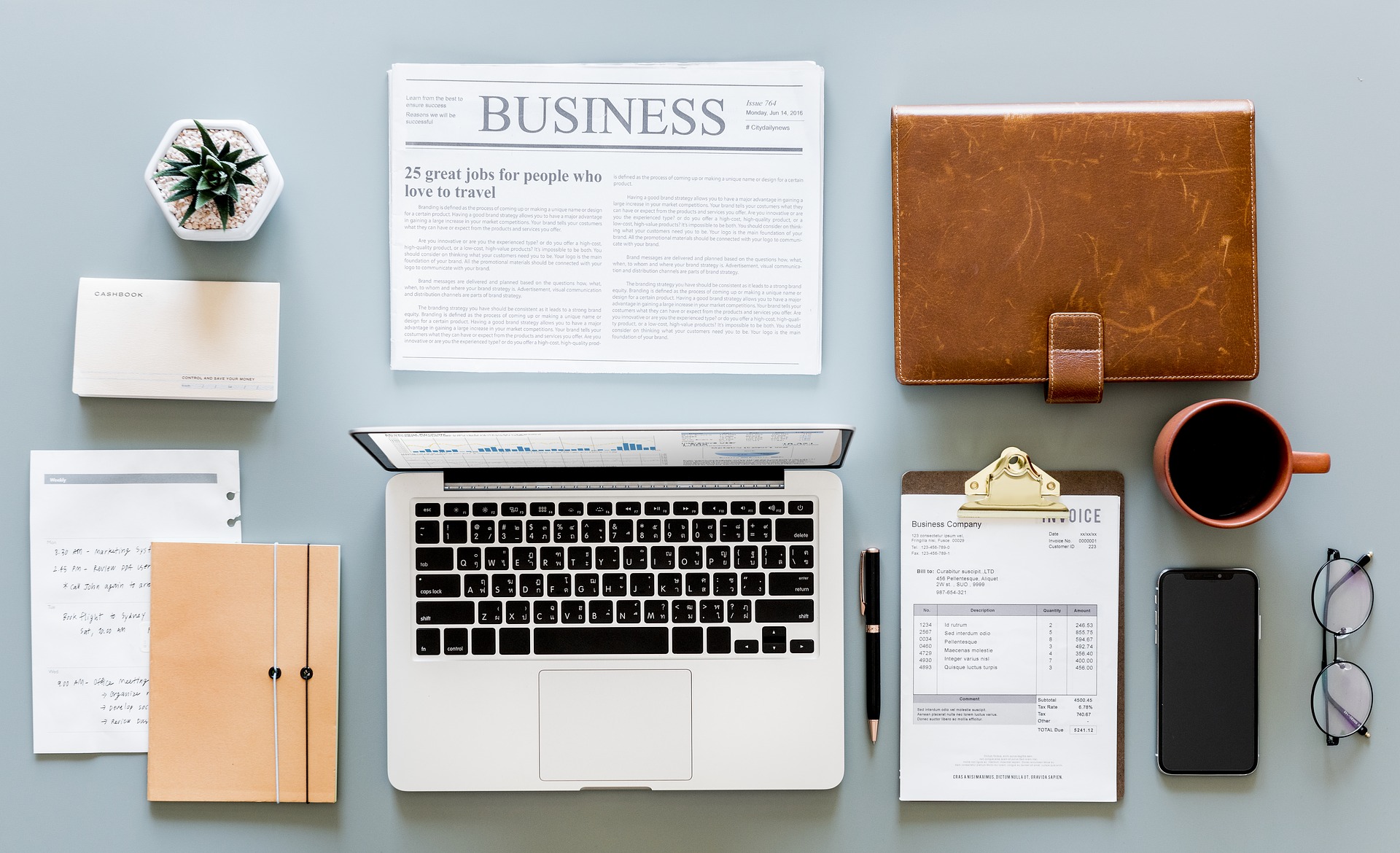 Table with newspaper, computer, glasses, checklist and other papers